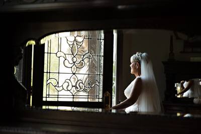 This is a photo taken in a mirror. The bride stands next to two very ornate wooden doors and peeks outside at her autumn wedding day. Her veil and tiara combo make this Southern Bride look like a princess on her wedding day. 